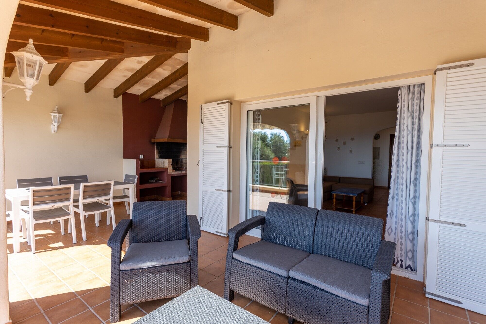 Un espacio de estar al aire libre con techo, amueblado con muebles de mimbre, una mesa y una chimenea.