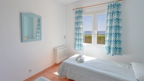 A bedroom with two beds, a window with curtains, a radiator, and a mirror on the wall. - Vacation Home "Villa Primavera" with Sea View and Pool (son bou, Alaior)