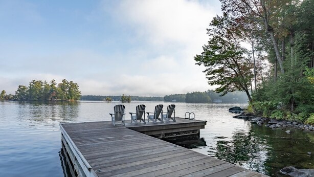 Een houten steiger die uitstelt in kalm water, met drie Adirondack-stoelen en een tafel op de steiger.