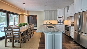 A modern kitchen with white cabinetry, stainless steel appliances, and a wooden dining area. - Beautiful open-concept cottage on Moon River! 10 Minute walk to Bala! (Bala)