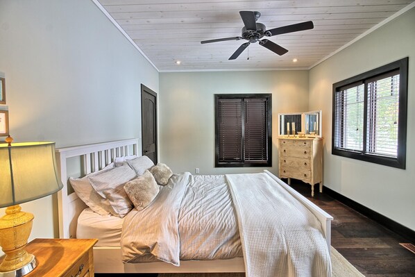 Un dormitorio con cama, cómoda, ventilador de techo, ventana con persianas y lámpara.
