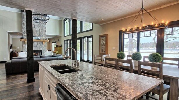 A spacious kitchen with a granite countertop, a built-in dishwasher, and a dining area with wooden chairs and a table. - Beautiful open-concept cottage on Moon River! 10 Minute walk to Bala! (Bala)