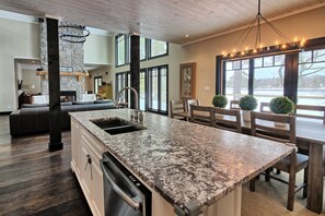 Una cocina amplia con encimera de granito, lavavajillas integrado y zona de comedor con sillas y mesa de madera.