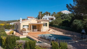 A Mediterranean-style villa with a swimming pool, outdoor seating, and a view of the surrounding hills. - Vacation Home "Villa Llebeig" Near the Beach with Sea View and Pool (San Jaime Mediterráneo)