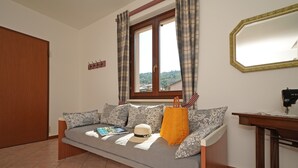 A room with a sofa, a window with curtains, a mirror, and a sewing machine.