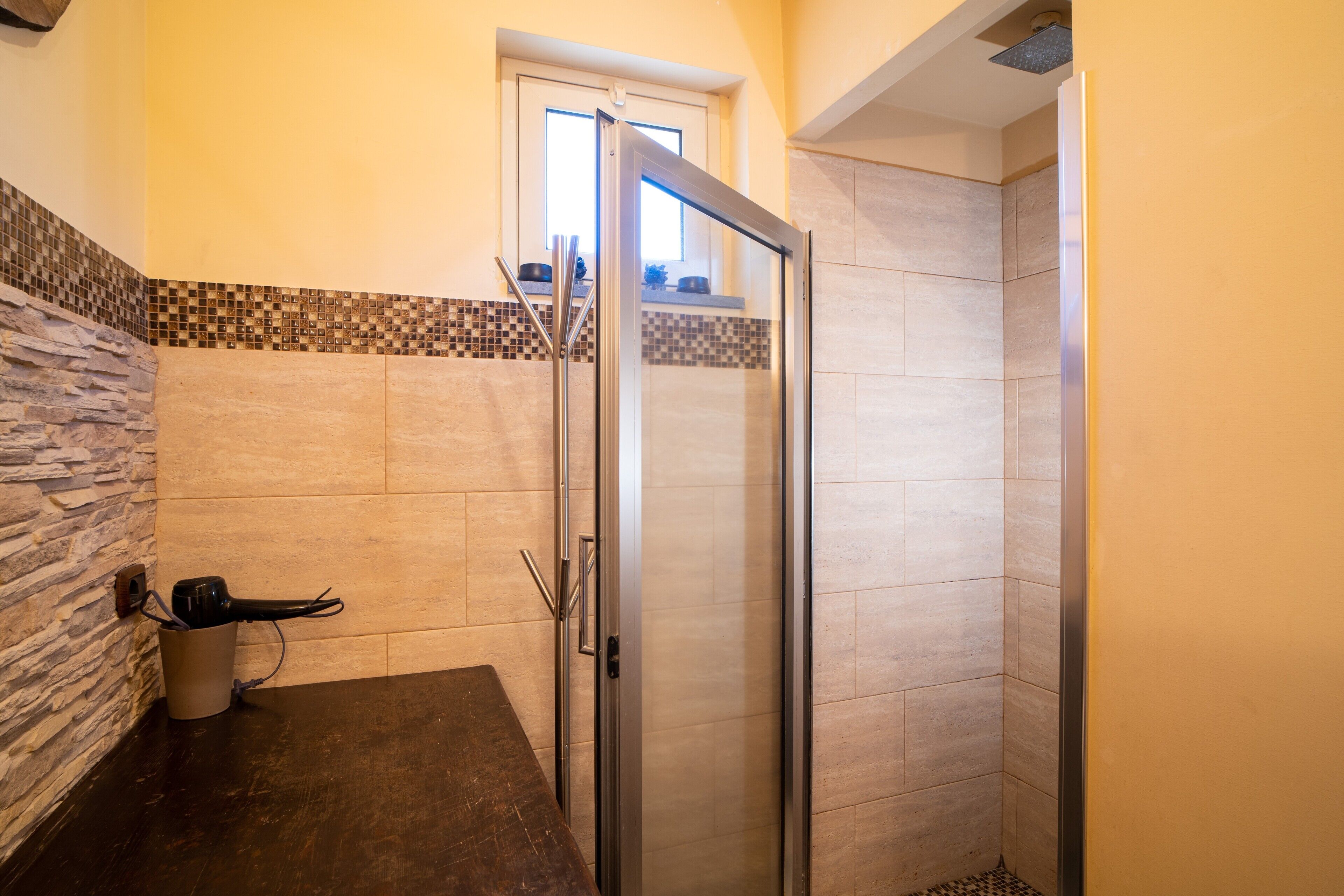 A bathroom with a glass shower door, a stone accent wall, and a tiled floor.