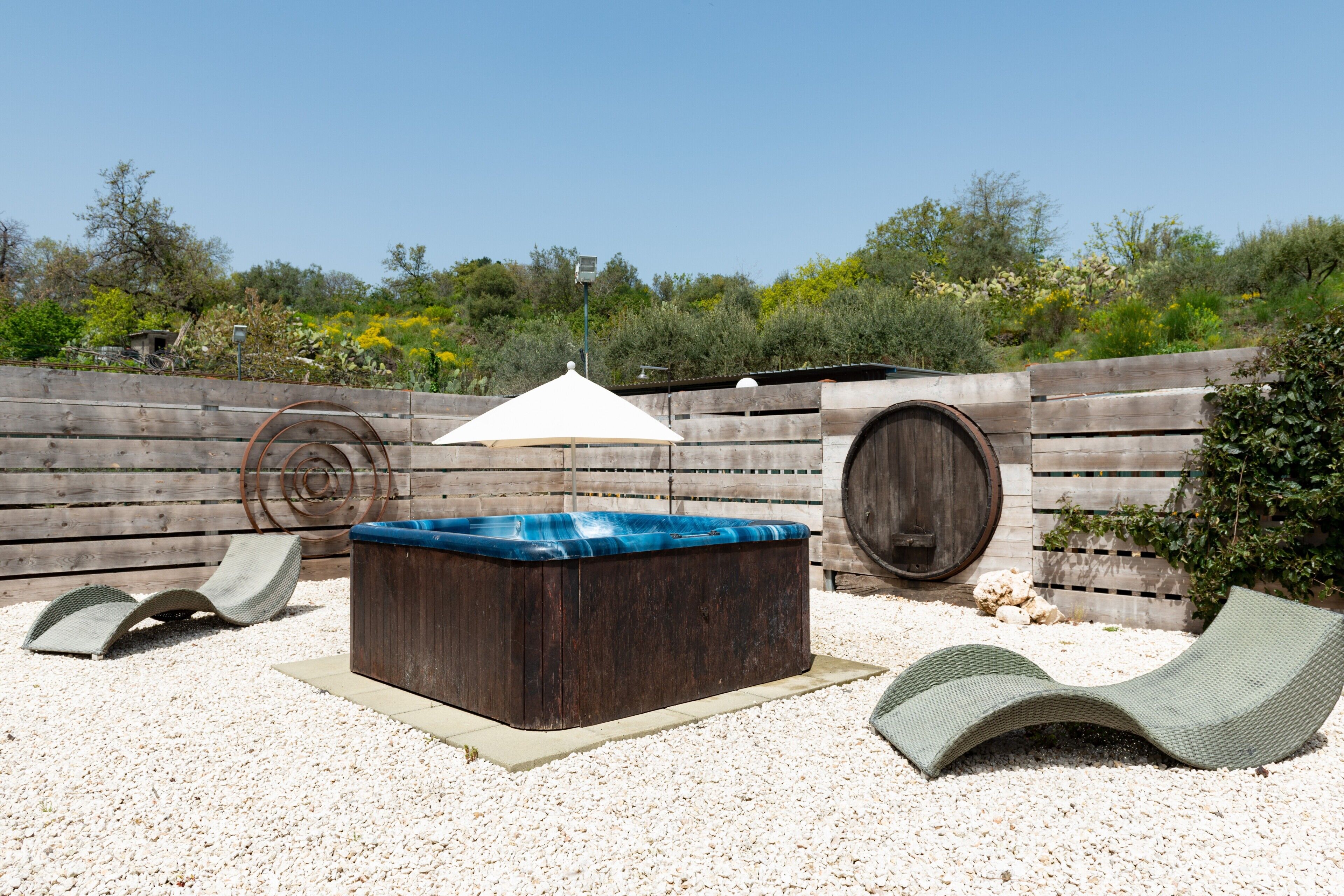 Eine Holzterrasse mit Whirlpool, Liegestühlen und einer Pergola.