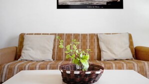 Un panier en osier contenant une plante, posé sur une table blanche devant un canapé à rayures agrémenté de deux coussins.