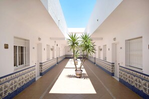 A corridor with tiled walls, potted plants, and doors with numbers.