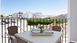 Un balcon avec des fauteuils et une table en osier, donnant sur un parking et des immeubles.
