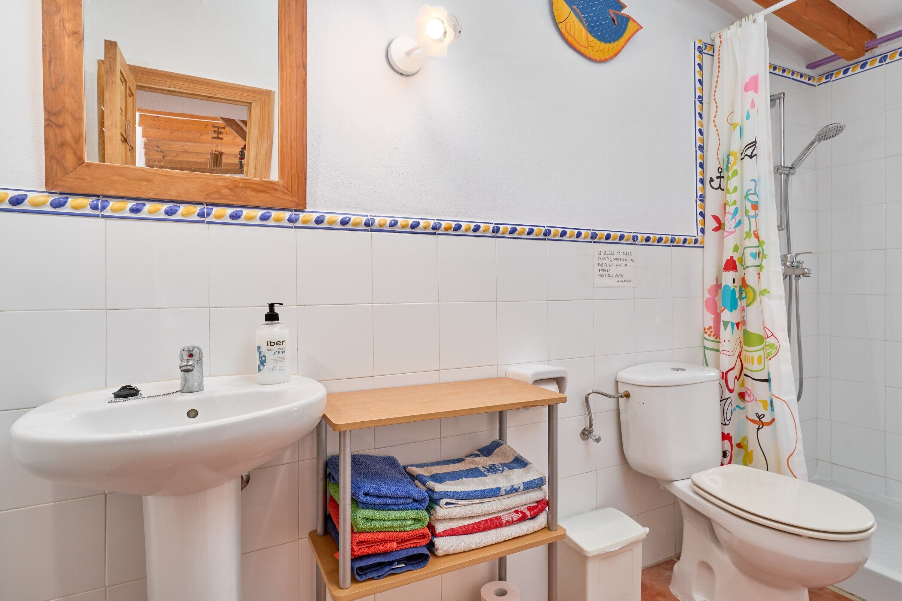 A bathroom with a sink, toilet, shelf with folded towels, and a shower curtain.