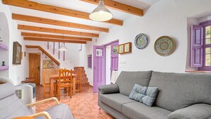 A living room with a grey sofa, wooden beams, a staircase, and a purple door. - Holiday Home 'Casa Rural El Tesillo' with Mountain View and Wi-Fi (Canillas de Aceituno)