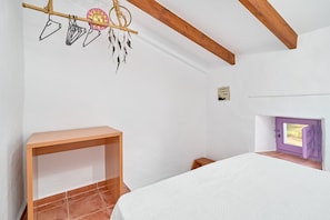 A bedroom with a bed, a wooden bench, a hanging dreamcatcher, and a door with a view.