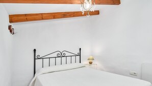 A bedroom with a bed, a nightstand with a lamp, a wooden beam ceiling, and a white wall. - Holiday Home 'Casa Rural El Tesillo' with Mountain View and Wi-Fi (Canillas de Aceituno)