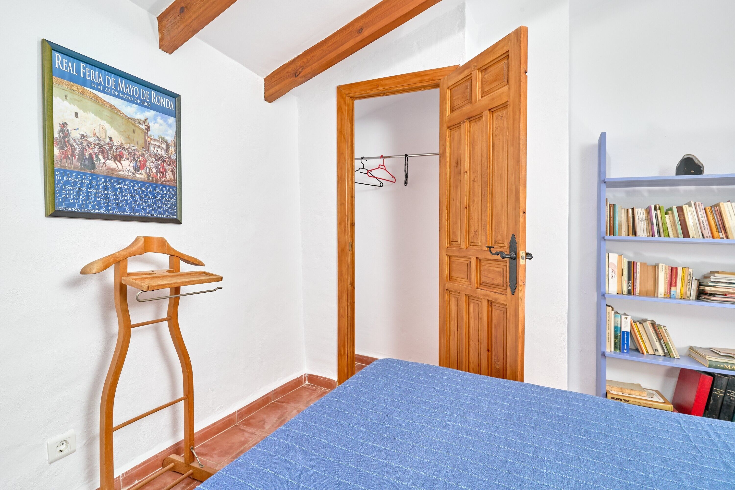 Una habitación con una cama, un tendedero de madera, una puerta, una estantería y un póster en la pared.