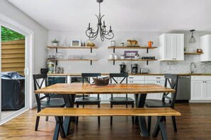 Cozinha moderna com mesa de jantar de madeira, cadeiras pretas, armários brancos e um lustre pendente.