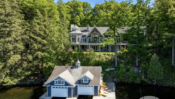 A large house with a dock extending into a lake, surrounded by dense trees. - Gorgeous 7 Bed, 6 Bath Family Cottage on Lake Rosseau! Muskoka Room! Pool Table! (Port Carling)