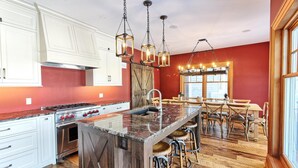 A kitchen with a central island, wooden bar stools, and a dining area with a table and chairs. - Gorgeous 7 Bed, 6 Bath Family Cottage on Lake Rosseau! Muskoka Room! Pool Table! (Port Carling)