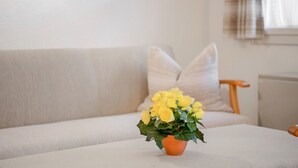 Sala de estar com sofá, um pequeno vaso laranja com flores amarelas e janela com cortinas.