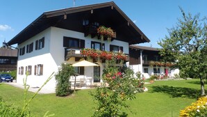 Um edifício de dois andares com telhado inclinado, varandas com floreiras e um gramado bem cuidado.