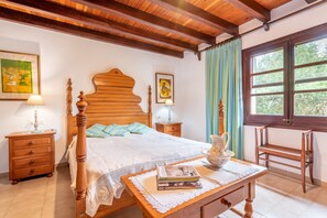 A bedroom with a wooden bed, bedside tables, a nightstand, a window with curtains, and a view of greenery outside. - Villa "Can Sol" with Private Pool and Large Garden in Pollensa (Pollensa)