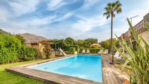 A rectangular swimming pool with a wooden deck, surrounded by greenery and a mountain backdrop. - Villa "Can Sol" with Private Pool and Large Garden in Pollensa (Pollensa)