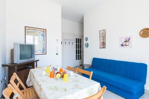 Un comedor con una mesa dispuesta para dos personas, un sofá azul y un televisor sobre un mueble de madera.