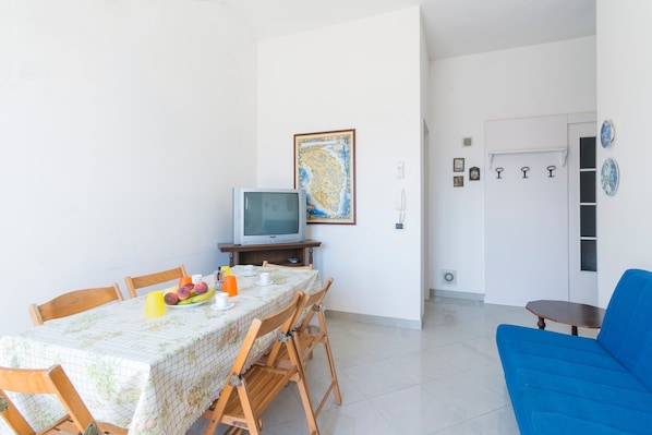 A dining area with a table set for two, a television, and a blue sofa.