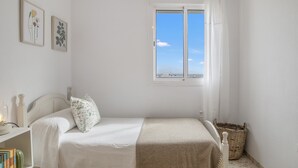 Ein Schlafzimmer mit Bett, einem Fenster mit Blick, einem Nachttisch mit Büchern und einem Wandbild.