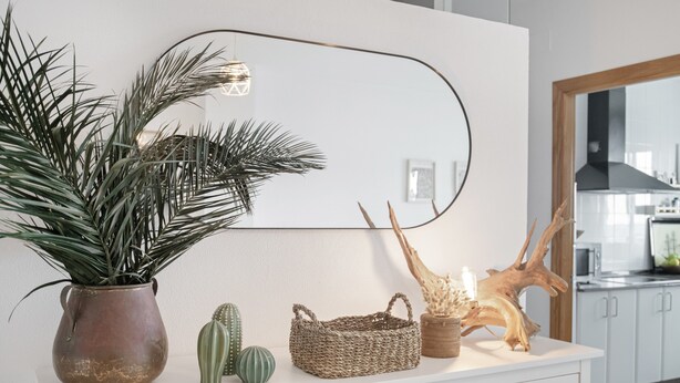 Ein weißes Schrankschrank mit einem Topfpflanzen, einem gewebten Korb und einer Holzskulptur.