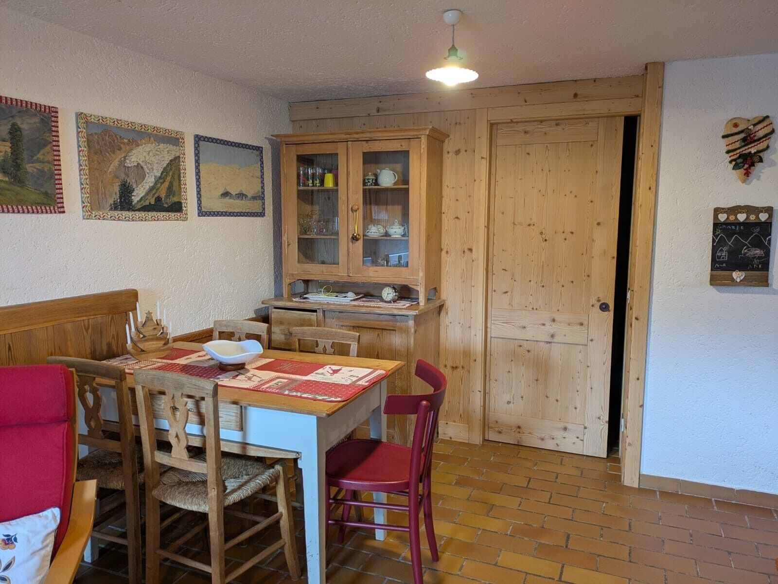 A dining area with a wooden table and chairs, a cabinet with glass doors, and a door with a heart-shaped decoration.