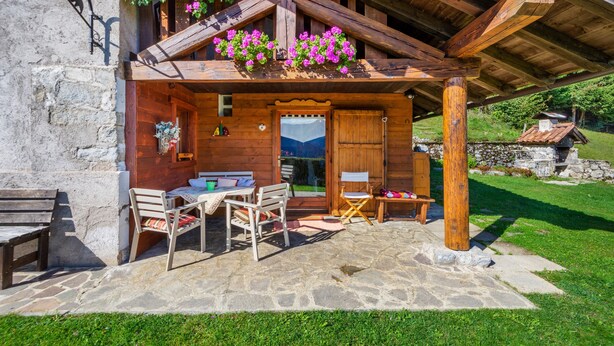 Una cabaña de madera con un patio de piedra, una mesa de madera con sillas y una ventana con vistas.