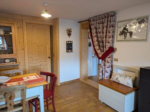 A cozy room with a wooden door, a table with a red tablecloth, a red chair, a bench with a cushion, and a wall-mounted picture.