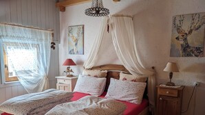 Un dormitorio con cama de madera, una mesita de noche con lámpara, una ventana con cortinas translúcidas y obras de arte en las paredes.