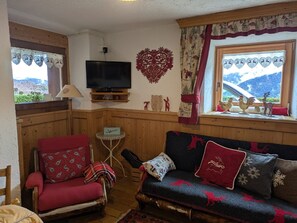 A cozy living room with a television, wooden paneling, a red armchair, a blue sofa with patterned cushions, and a decorative heart on the wall.