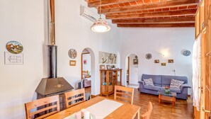 A dining area with a wooden table, chairs, a chandelier, and a wood-burning stove.