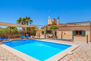 A swimming pool with lounge chairs, a lifebuoy, and a building with a tiled roof and balcony. - Charming Finca with Pool, Garden, Terrace, Air Conditioning & Wi-Fi (Santanyí)