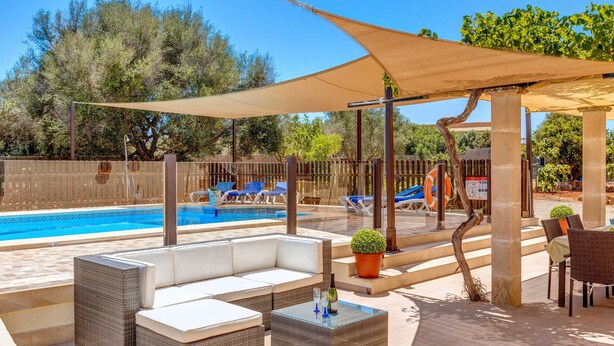 A poolside area with wicker furniture, a shaded umbrella, and a view of the pool.