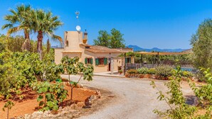 A villa with a paved driveway, a small garden, and a view of distant mountains.
