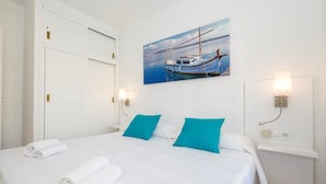 A hotel room with a bed, two pillows, a painting of boats, and a nightstand with a lamp. - Modern apartment in complex with pool - Girasols Gardens Sup (Son Bou)