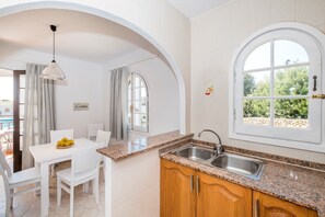 A kitchen with a granite countertop, white cabinets, a stainless steel sink, and a window with a view of greenery. - Modern apartment in complex with pool - Girasols Gardens Sup (Son Bou)