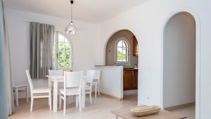 A dining area with a table and chairs, a kitchen with an archway, and a window with curtains. - Modern apartment in complex with pool - Girasols Gardens Sup (Son Bou)