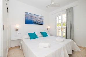 A double bed with white and teal bedding, a ceiling fan, a painting of a boat, and a window with curtains. - Modern apartment in complex with pool - Girasols Gardens Sup (Son Bou)