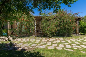 Un jardin avec un chemin de pierres, une pergola en bois et des plantes en fleurs.