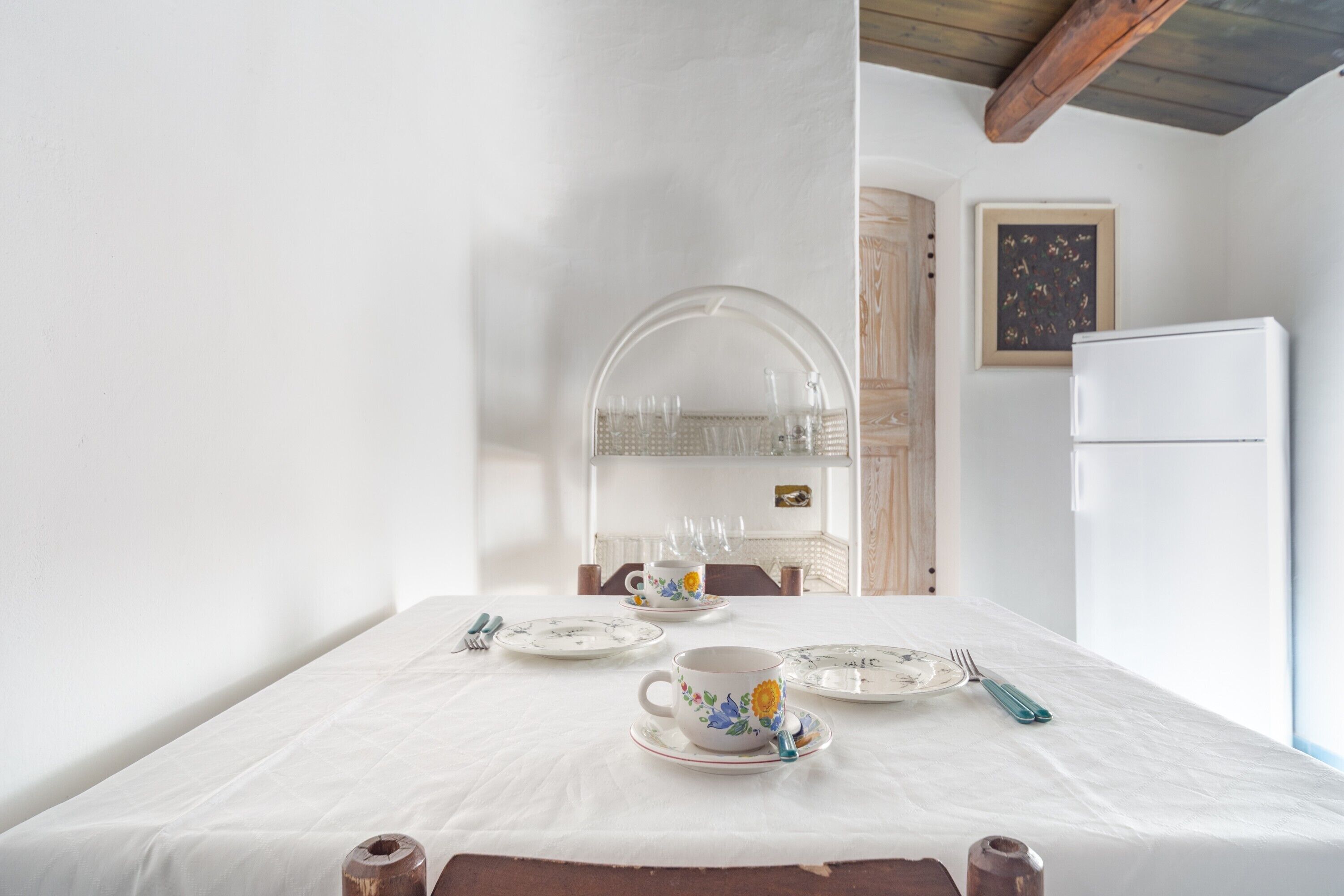 Une table à manger dressée avec des assiettes, des tasses et des couverts, un réfrigérateur et un buffet en bois à l’arrière-plan.