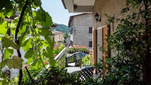 Un balcón con una silla, una mesa y vista a un edificio de pared de piedra y puerta de madera.