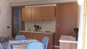 Una cocina compacta con armarios de madera, una mesa de comedor con sillas azules y una pequeña zona para café.