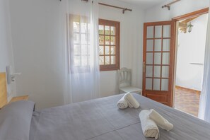 A bedroom with a bed, a chair, a wooden door, and a window with curtains.