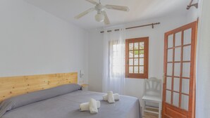 Ein Schlafzimmer mit einem Bett, einem Sessel, einer Holztür und einem Fenster mit Vorhängen.