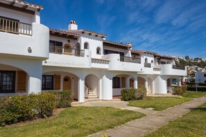 A white building with multiple balconies, arched doorways, and a clear sky.